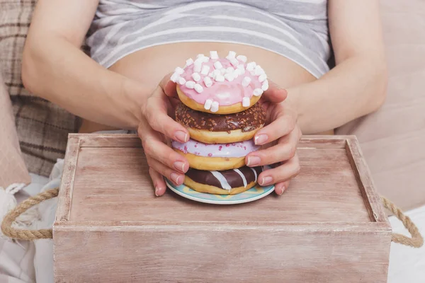 Беременная женщина с разными пончиками на деревянном подносе — стоковое фото