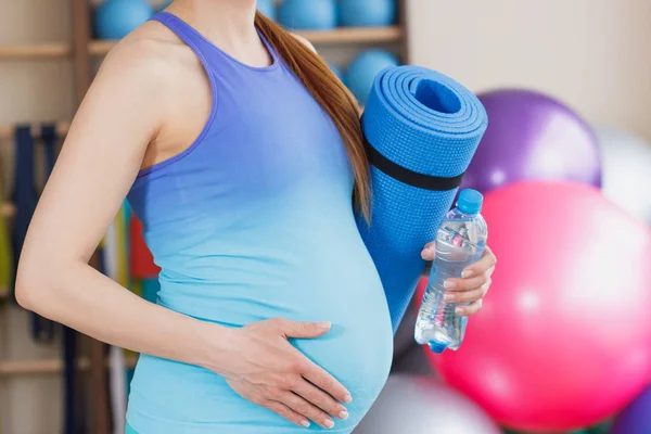 Těhotná žena sportovní s podložka pro jógu v ruce — Stock fotografie