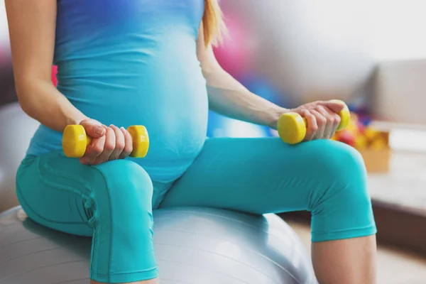 手にダンベルでスポーティな妊婦がボールに座っています。 — ストック写真