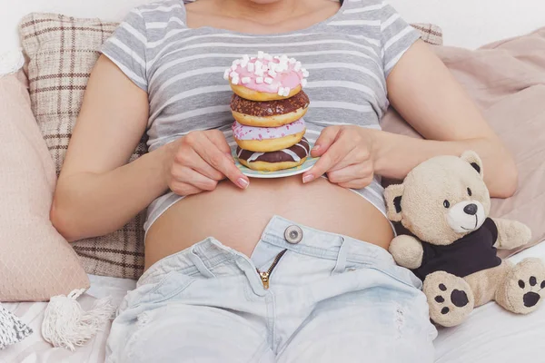 Беременная женщина с разными пончиками на тарелке — стоковое фото