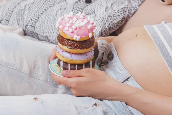 Zwangere vrouw met verschillende donuts op de plaat — Stockfoto