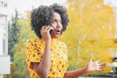 Genç gülümseyen koyu tenli kadın rahat giysiler giymiş telefonu yla konuşurken