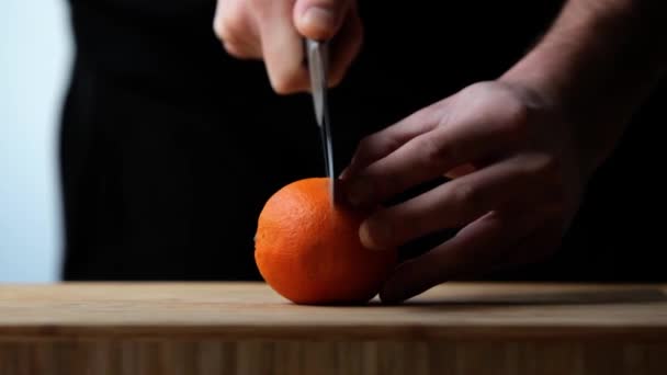 Ein Mann Schneidet Eine Orange Auf Das Holzbrett Der Küche — Stockvideo