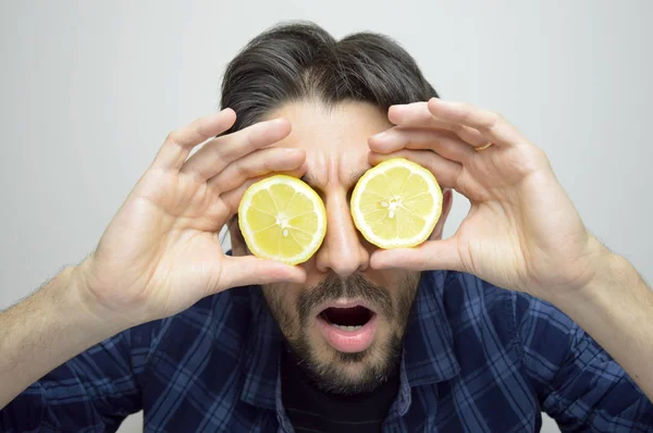 Jonge man die betrekking hebben op zijn ogen met citroenen en ontdek een nieuwe zaak verrast / nieuw product — Stockfoto