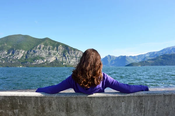 Młoda kobieta siedzi na ławce z widokiem na jezioro — Zdjęcie stockowe