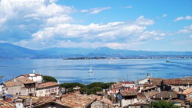Bir Desenzano Del Garda, İtalya - 15 Mayıs 2017: panorama eski şehir çatılar, dağlar, beyaz bulutlar ve yelkenli gölde, Desenzano del Garda, İtalya ile Desenzano Kalesi: Garda Gölü üzerinde şaşırtıcı