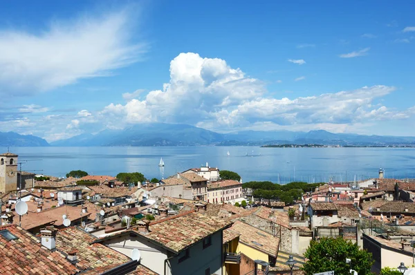 Desenzano Del Garda, Italien - 15 maj 2017: fantastisk panorama från Desenzano slott vid Gardasjön med gamla stadens tak, berg, vita moln och segelbåtar på sjön, Desenzano del Garda, Italien — Stockfoto