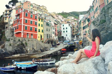 Arkadan Görünüm kırmızı taşlar üzerinde gibi İtalyan Rivierası manzara, aynasızlar kamera ile fotoğraf çekme deniz kızı Riomaggiore, Cinque Terre, İtalya oturan kız kılığında. Vintage filtre