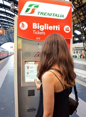 MILAN, ITALY - JULY 19, 2017: girl buying a ticket via self-service ticket machine in central railway station of Milan, Italy clipart