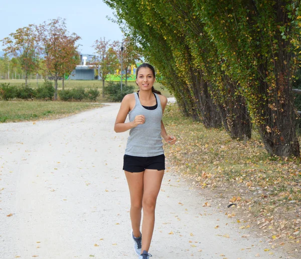 Uma jovem atleta desportiva activa a correr no parque. Smiling atleta corredor de treinamento ao ar livre . — Fotografia de Stock