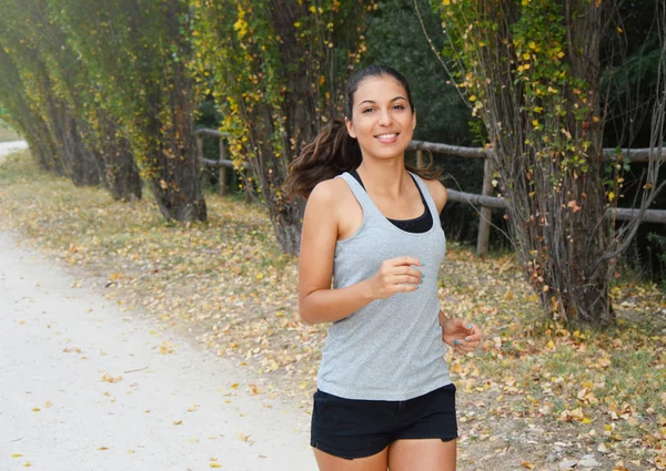 Chica sonriente corriendo en el parque. Hermosa joven fitness mujer corriendo al aire libre . —  Fotos de Stock