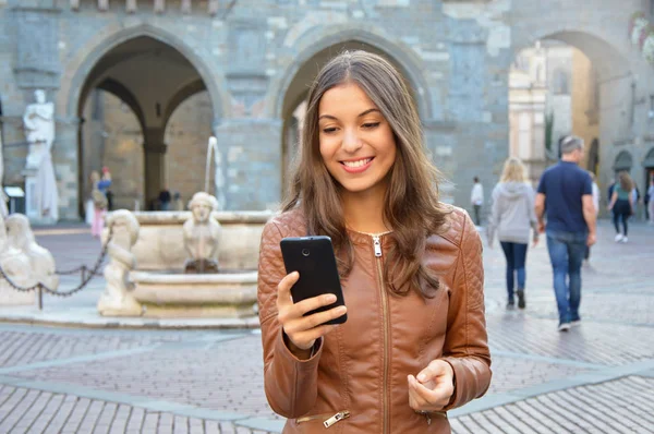 Kentsel arka planda akıllı telefon kullanarak kahverengi ceket ile güzel kız