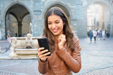 Akıllı telefon kullanan açık havada heyecanlı genç kadın