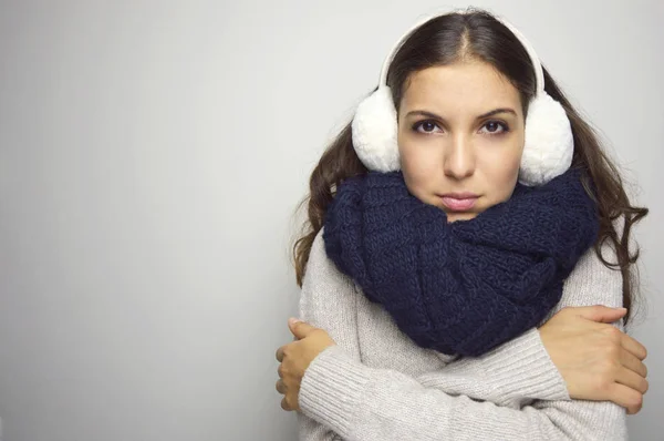 Shivering young woman being cold wearing earmuffs, sweater and scarf. Copy space.
