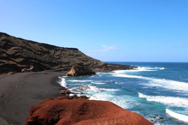 El Golfo Koyu'nun nefes kesen manzarası: kırmızı zemin, mavi deniz ve arka plan, Lanzarote, Kanarya Adaları volkanik Dağları ile siyah kum