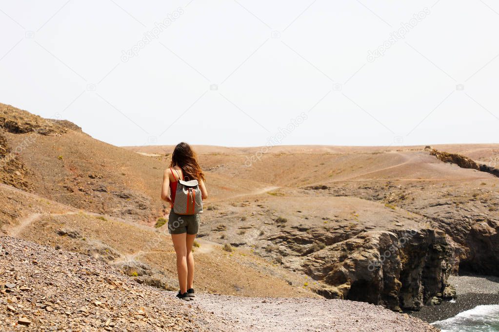 Hiking female walking on Lanzarote martian desertic landscape. Back view of young woman exploring volcanic island of Lanzarote, Canary Islands.