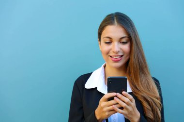 Genç, dikkati dağılmış iş kadını vaktini sosyal ağda harcıyor. Açık havada mavi arka planda duran akıllı telefonla yazı yazıyor..