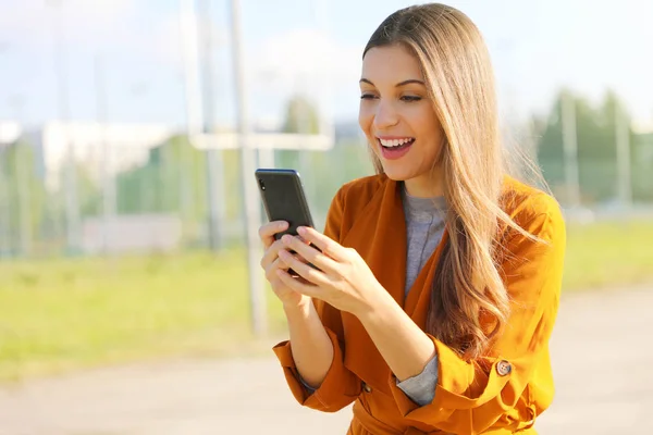 Feliz hermosa mujer caminando y escribiendo o leyendo mensajes SMS en línea en un teléfono inteligente . —  Fotos de Stock