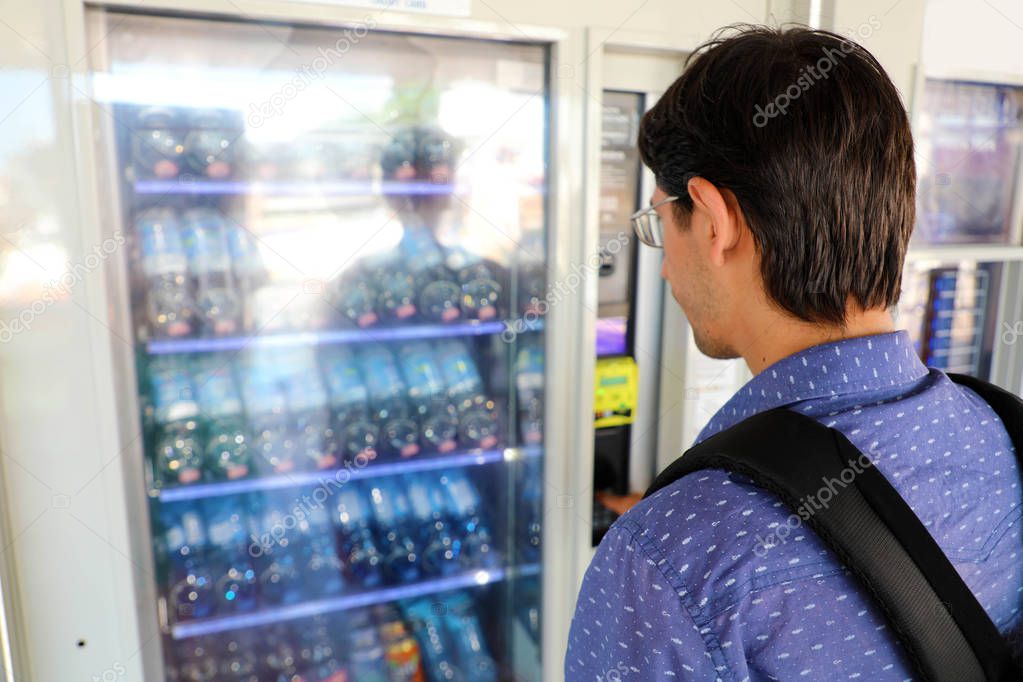 Young male backpacker tourist choosing a snack or drink at vending machine. Vending machine with man.