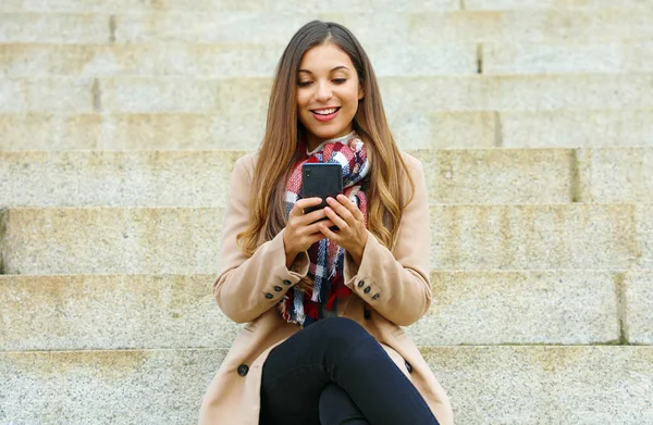 Sonriente joven bonita mujer usando el teléfono inteligente sentado en las escaleras del parque público . —  Fotos de Stock