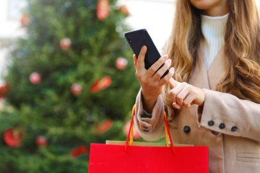 Alışveriş yapan kadın internetten alışveriş yapmak ve Noel zamanı çanta taşımak için akıllı telefon kullanıyor..