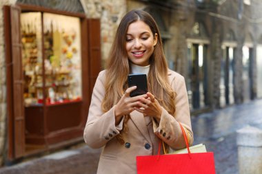 Alışveriş yapan kadın kışın eski şehir sokağında akıllı telefonuyla internetten alışveriş yapıyor..