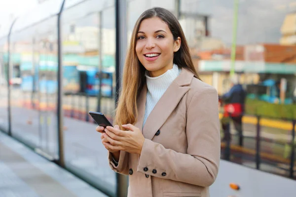 People and public transport. Happy beautiful woman holding cellular at tram stop.