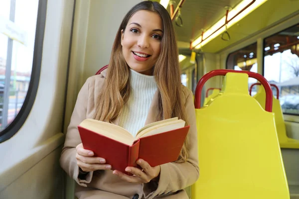 Schöne junge Frau sitzt in der Straßenbahn gefangen und überrascht beim Lesen ihres Buches blickt in die Kamera. — Stockfoto