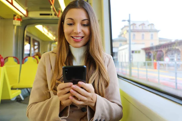Gente en transporte público. Sonriente mensajería de mujer joven con teléfono inteligente sentado en el tranvía . — Foto de Stock