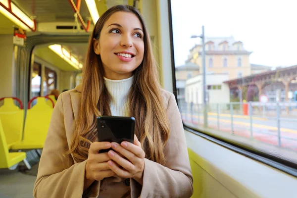 Gente en transporte público. Sonriente hermosa mujer joven sosteniendo el teléfono móvil mirando a través de la ventana en el tranvía . — Foto de Stock