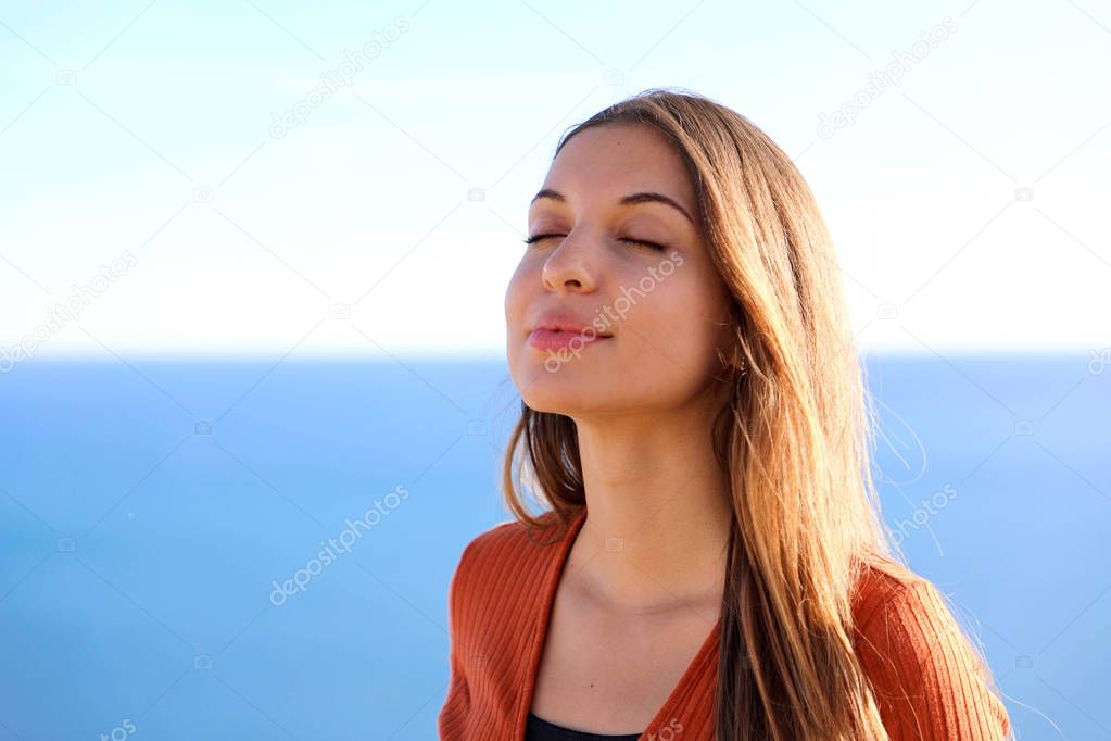 Close up of beautiful relaxed girl breathing and smiling with blue sea on the background.