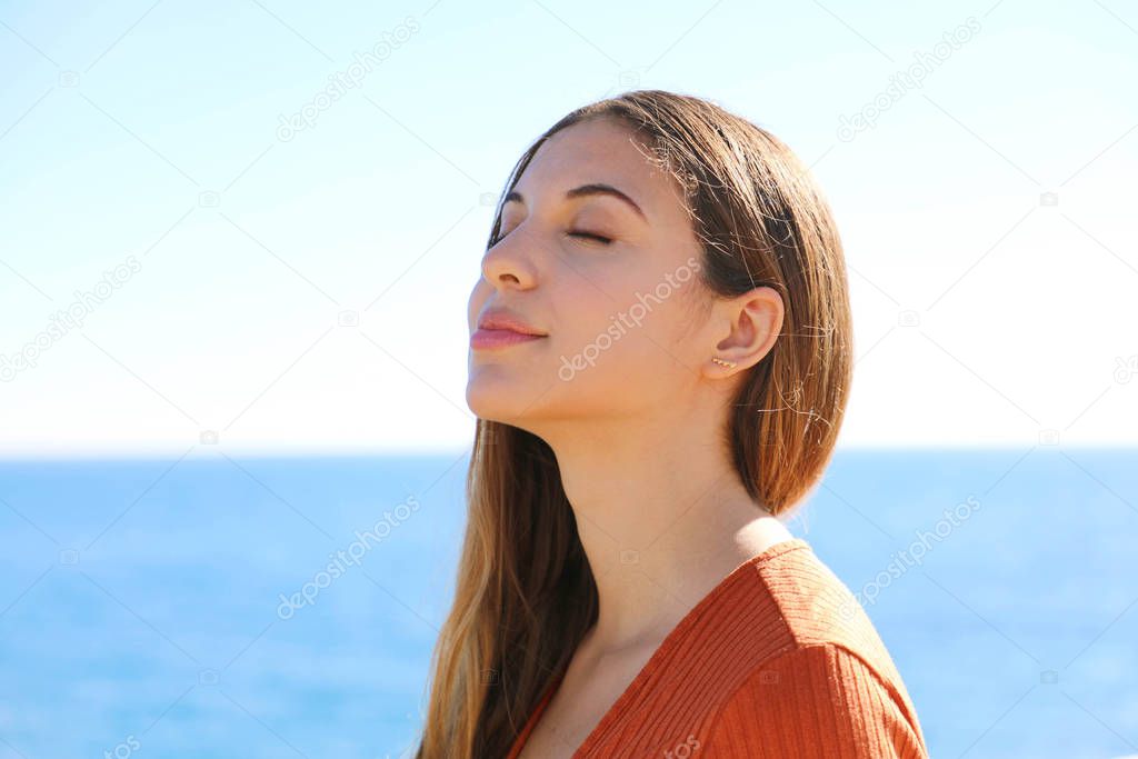 Woman profile portrait breathing deep fresh air on the beach with the ocean on background.