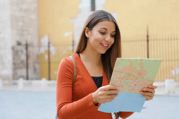 Travel girl visiting city searching direction on map. Happy cheerful female tourist exploring new city searching road or location on map during vacation.