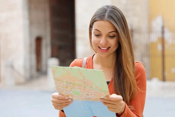 Путешествующая девушка посещает город в поисках направления на карте. Счастливая веселая женщина-туристка, исследующая новый город в поисках дороги или местоположения на карте во время отпуска . — стоковое фото