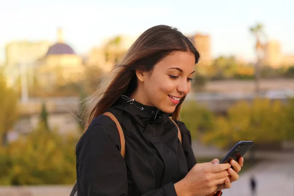 Smiling beautiful woman typing messaging with smarphone outdoor at sunset . — стоковое фото