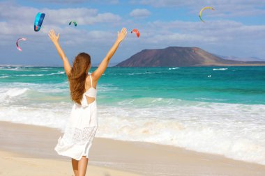 Kollarını kaldırıp rüzgardan hoşlanan genç bir kadın ve uçurtma uçuran insanlar, Corralejo Dunes plajı, Fuerteventura, Kanarya Adaları