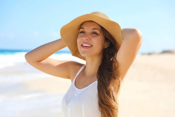 Uśmiechnięta młoda kobieta w słomkowym kapeluszu rozkoszująca się wiatrem na plaży — Zdjęcie stockowe