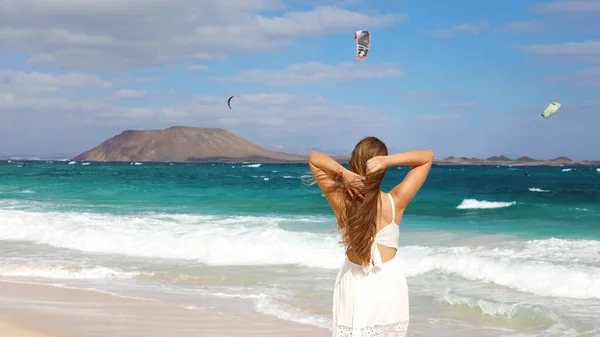 Γυναίκα σε λευκό sundress αναζητούν άτομα που κάνουν kitesurfering αθλητισμού, ενώ το περπάτημα στην παραλία Corralejo Dunes, Fuerteventura, Κανάρια Νησιά — Φωτογραφία Αρχείου