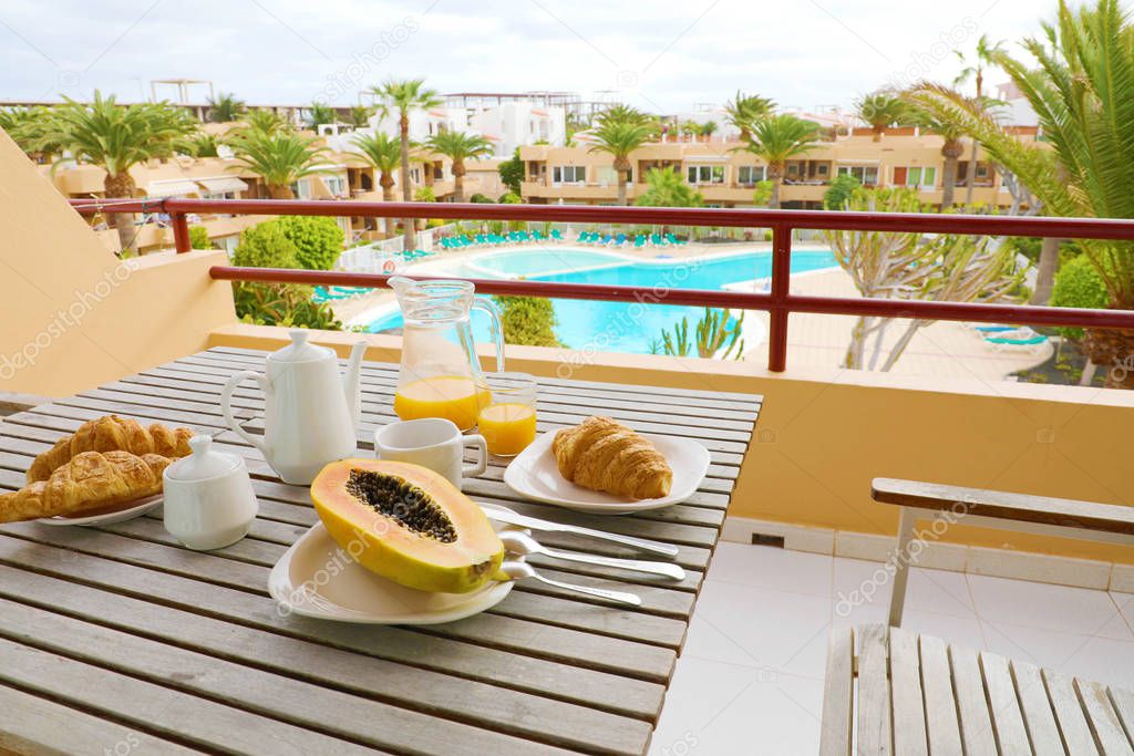 Hotel room breakfast on balcony view of swimming pool and palm trees. Vacation travel morning food breakfast in luxury resort outside.
