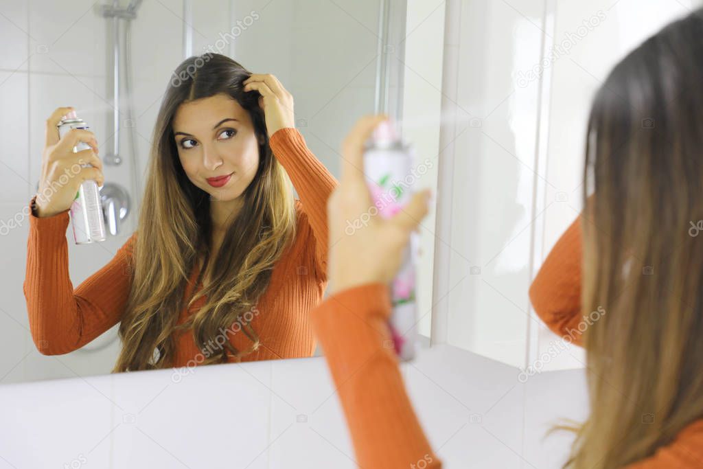 Young woman applying dry shampoo on her hair. Fast and easy way to keep hair clean with dry shampoo.