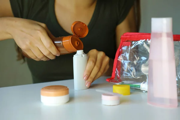 Femme a versé du liquide dans de petites bouteilles préparant un kit de voyage pour le transport en avion. Trousse de voyage transport cosmétique sur avion concept . — Photo