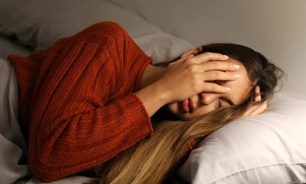 Young woman has a difficulty falling asleep. Girl with insomnia or headache cover her face with hand. — Stock Photo, Image