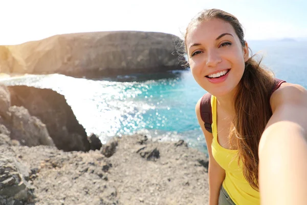 プラヤパガヨの風景で自撮り写真を撮る観光客の女性。幸せな美しい女の子は、スペインのカナリア諸島のプレヤパパガヨビーチとランサローテの風景の自画像を取ります. — ストック写真