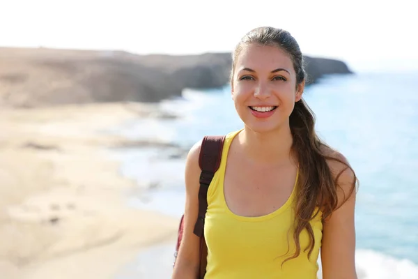 Portrait of happy hiker woman standing on the top of viewpoint looking at camera with blurred natural landscape. Travel and active lifestyle concept.