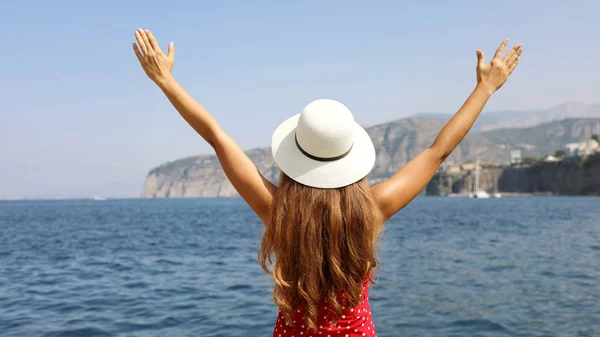 Красива молода жінка з капелюхом і піднятими руками дивиться на дивовижне панорамне село Сорренто на Соррентінському півострові (Італія). — стокове фото