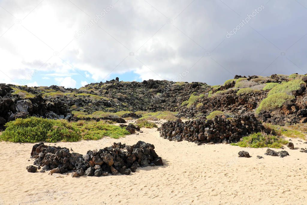 Stones shelters on the sand to protect from strong winds. Human nest made with volcanic rocks for wind protection on Caleton Blanco beach, Lanzarote, Canary Islands.