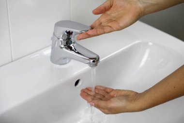 COVID-19, Novel Coronavirus 'a (2019-nCoV) karşı evdeki banyo lavabosunda ellerini yıkıyor. Kadın elleri sıcaklığı kontrol ediyor. Suya elle dokunuyor. Antiseptik, Hijyen ve Sağlık Konsepti.