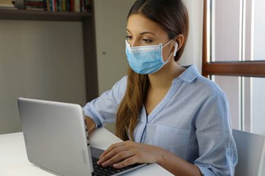 COVID-19 Pandemic Coronavirus Ev Bilgisayarından E-Öğrenci Maskesi Çalışması. Virüs hastalığı SARS-CoV-2 için evden eğitim gören genç bir kadın karantina altında. Akıllı okul konsepti.