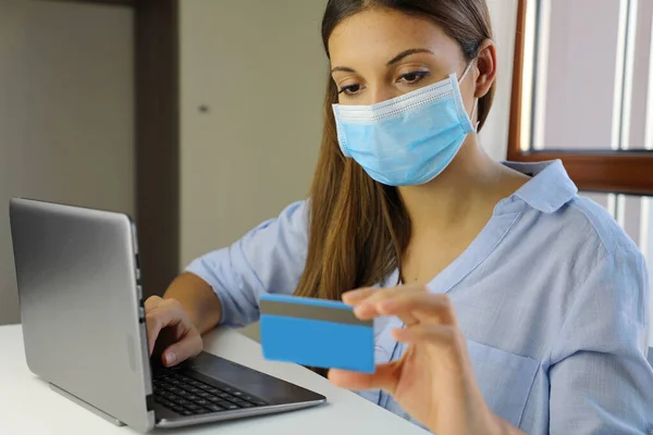 COVID-19 Pandemic Coronavirus E-commerce Mask Girl Buying with Laptop. Young woman with mask buying online with credit card during home quarantine for virus disease 2019-nCoV.