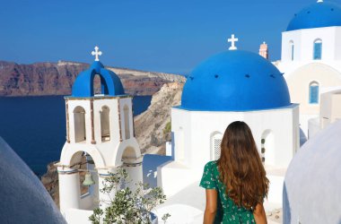 Yunanistan 'da turizm. Gezgin turist kızın Oia, Santorini 'nin mavi kubbeleriyle ünlü beyaz köyü ziyaret edişinin arkası. Avrupa seyahatleri.